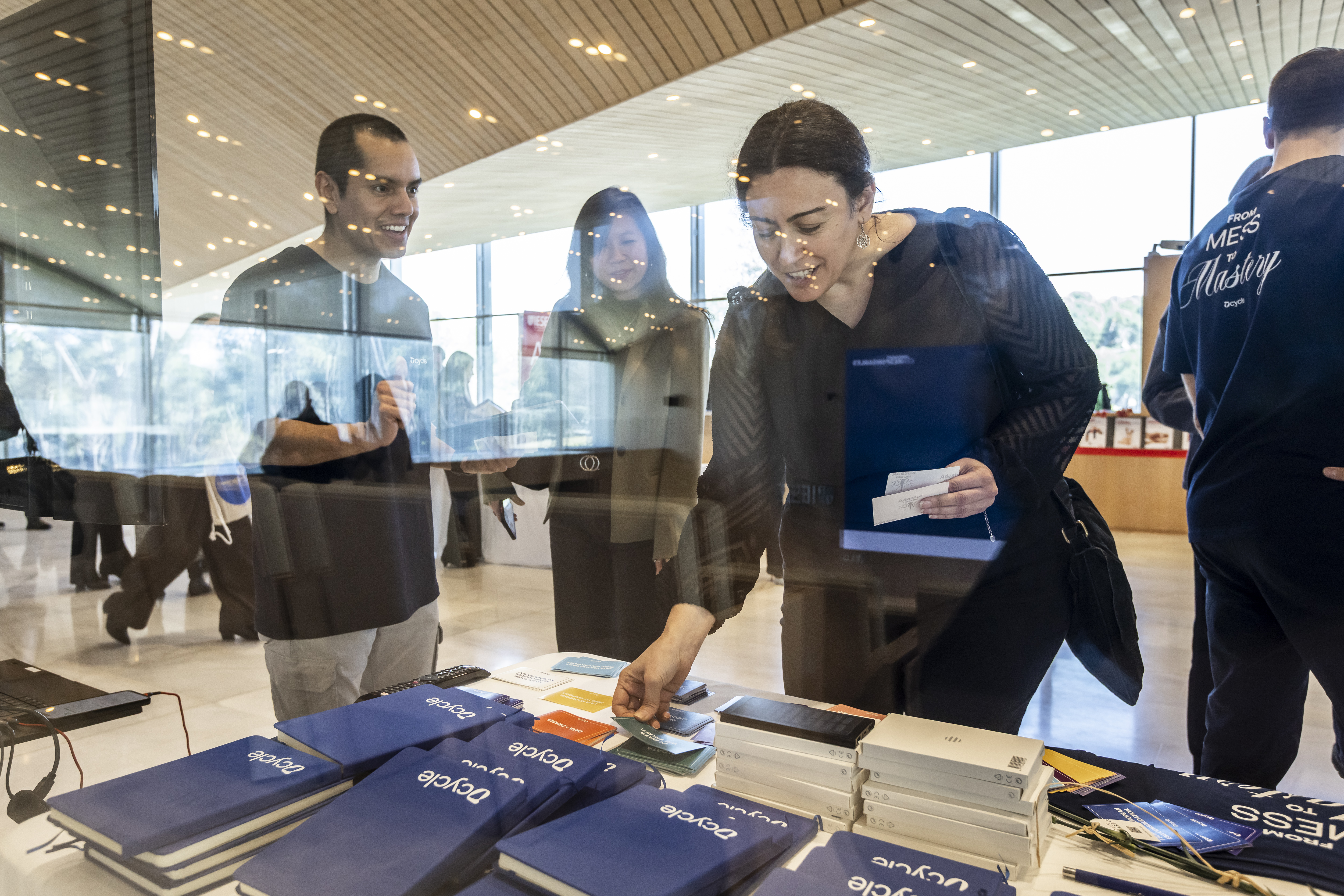 Asistentes mirando libretas y merchandising de Dcycle a traves del cristal del stand