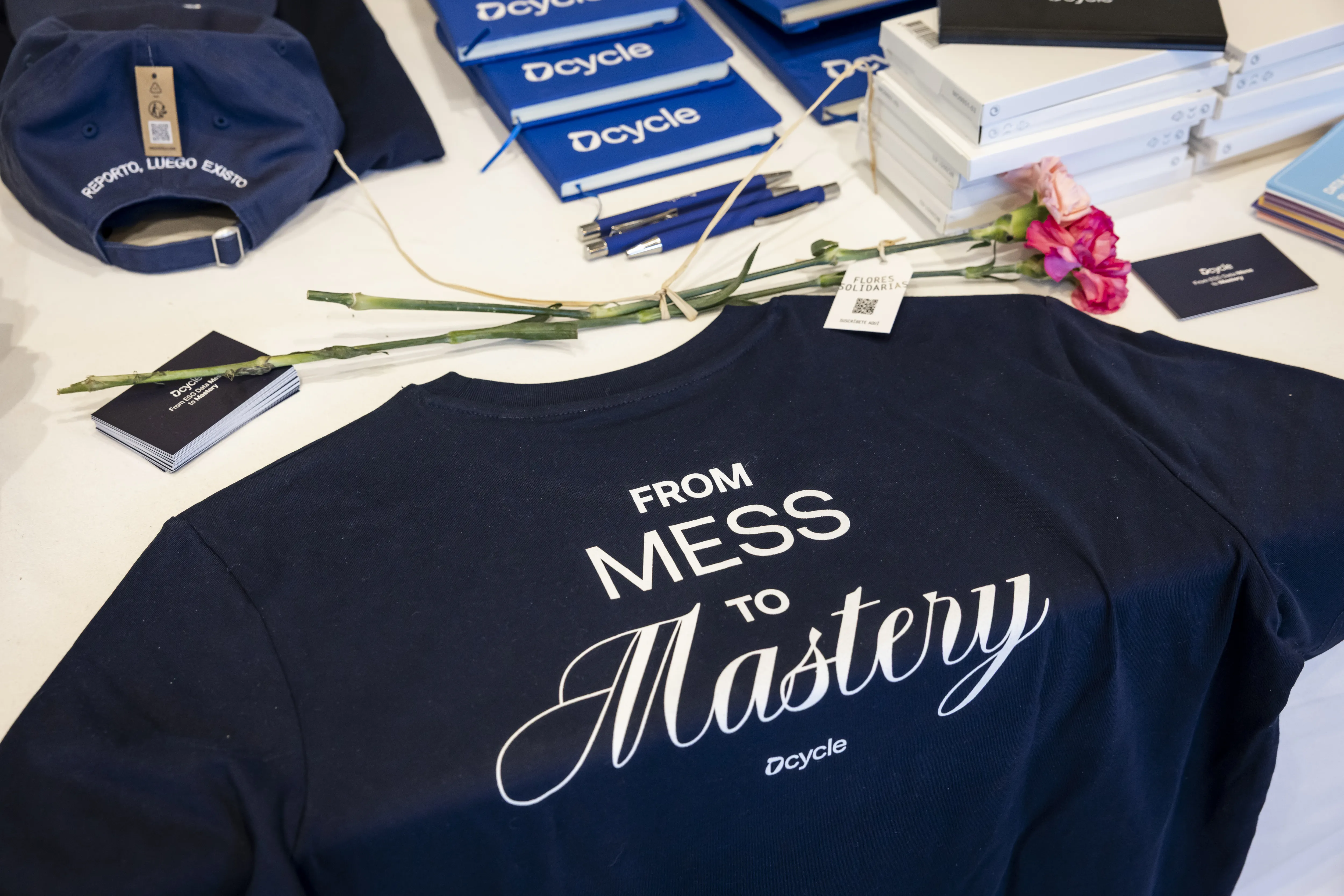 Dcycle branded merchandise table with From Mess to Mastery shirts, caps, and notebooks